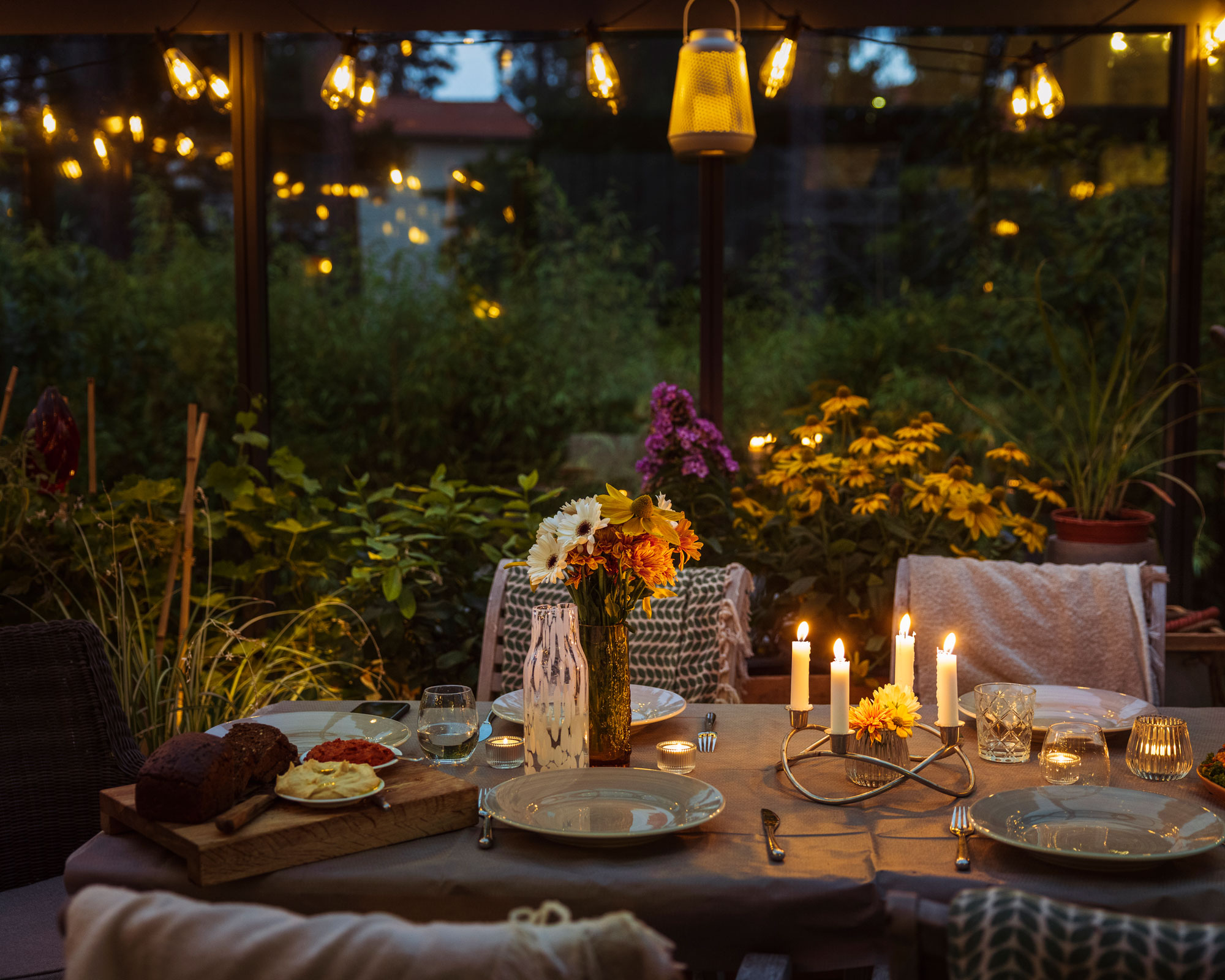 greenhouse with string and lantern lighting and outdoor dining area with table and place settings