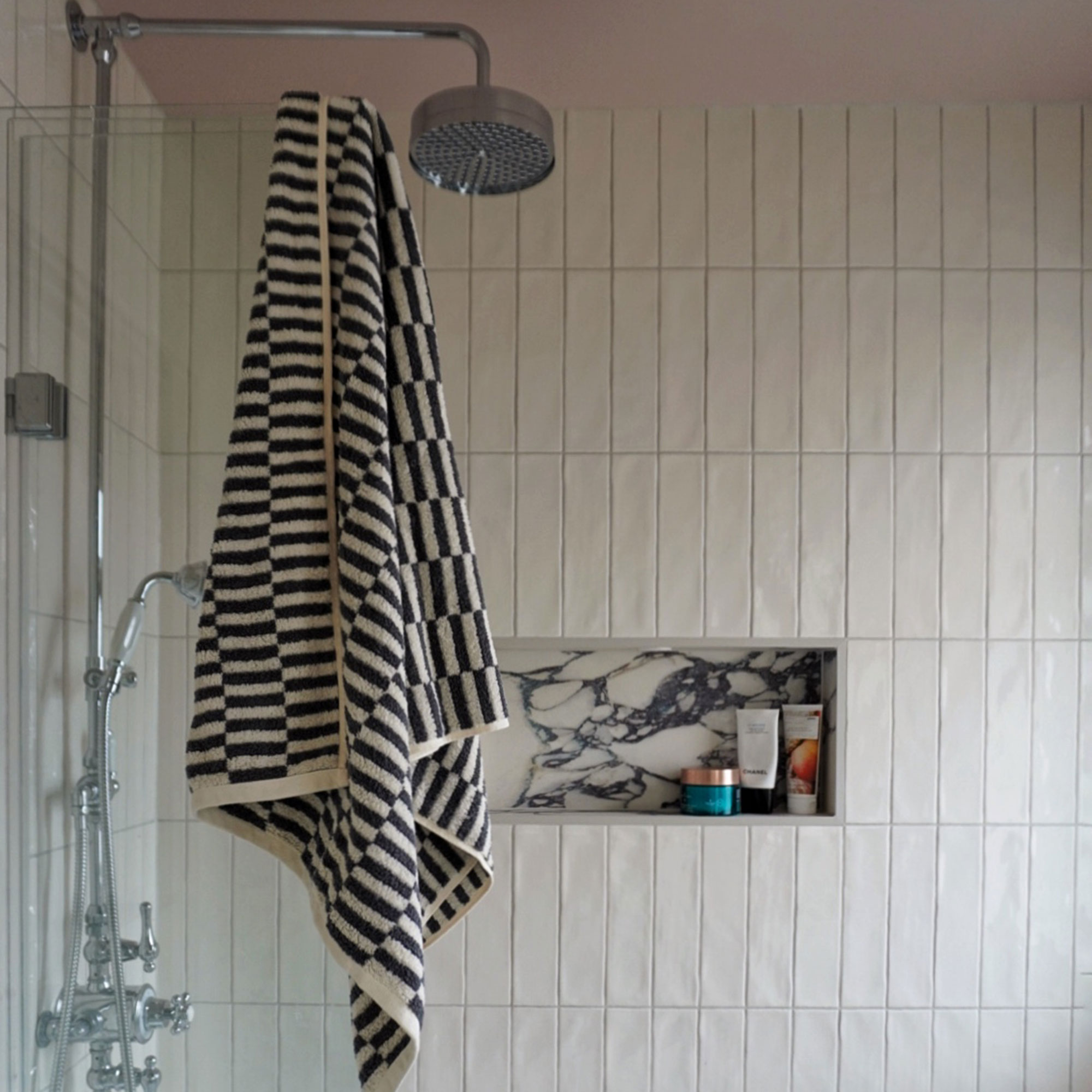 Neutral bath-shower enclosure tiled vertically with marble inset shelving