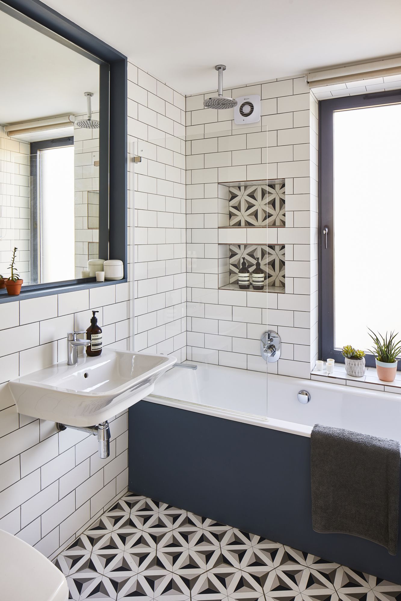 Une salle de bain familiale avec des carreaux muraux metro blancs, des carreaux de sol à motifs monochromes et une baignoire - douche avec panneau bleu profond peint