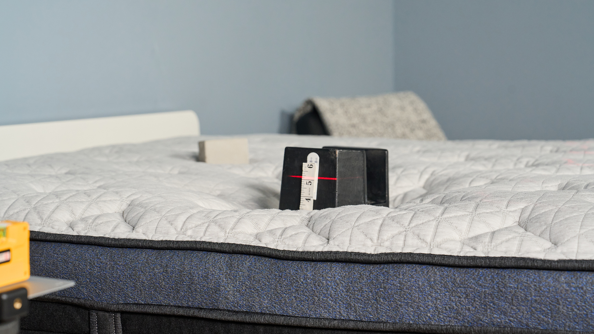 A close up of a 25kg weight balanced in the hip area of a mattress on the Helix Midnight Luxe. A laser is pointing at a tape measure on the side of the weight, to check the sinkage and help understand pressure relief