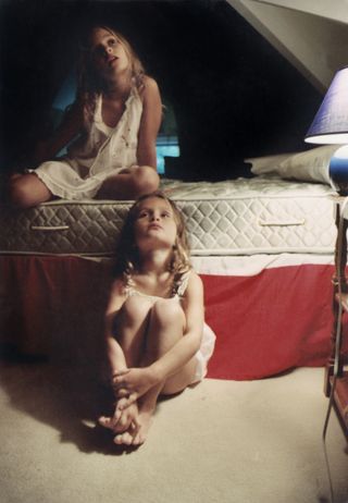 a still from photographer beth garrabrant's book of two young girls sitting next to a mattress in a dark bedroom