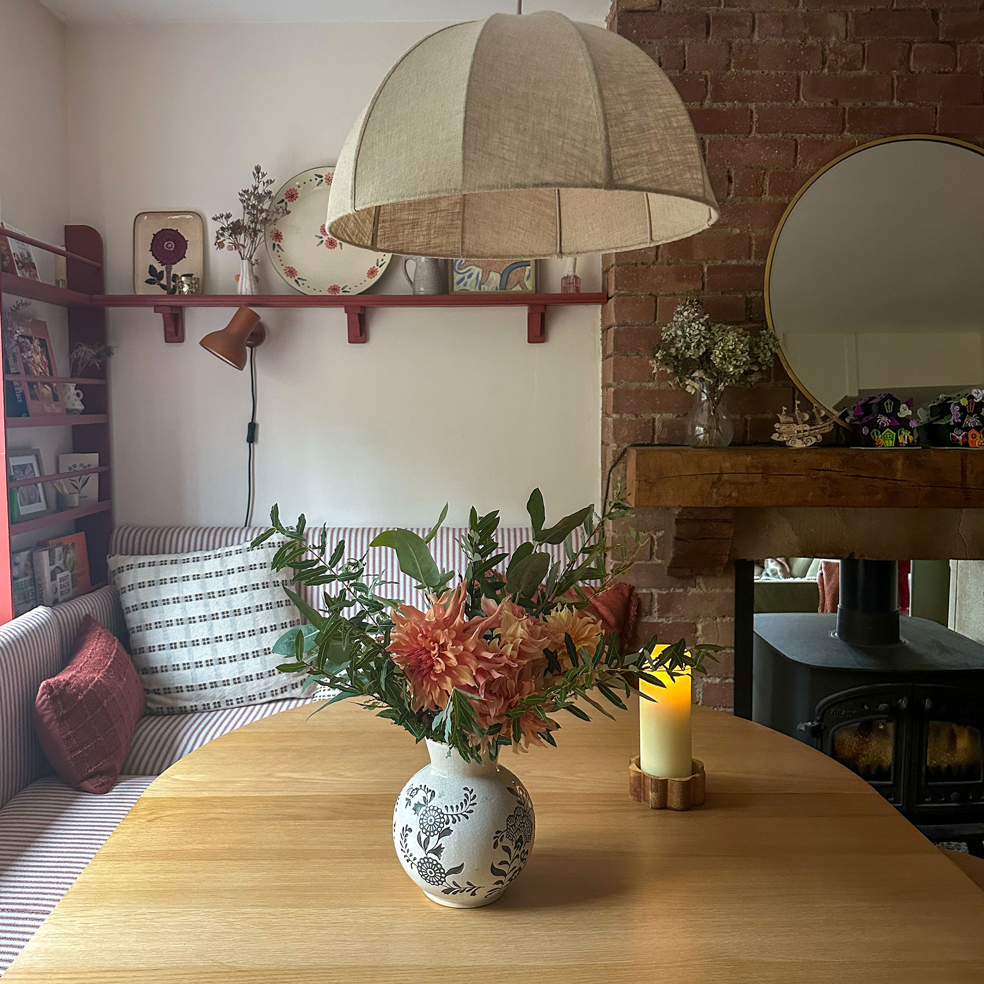 Wooden kitchen table with vase of fresh flowers underneath linen shaded pendant light