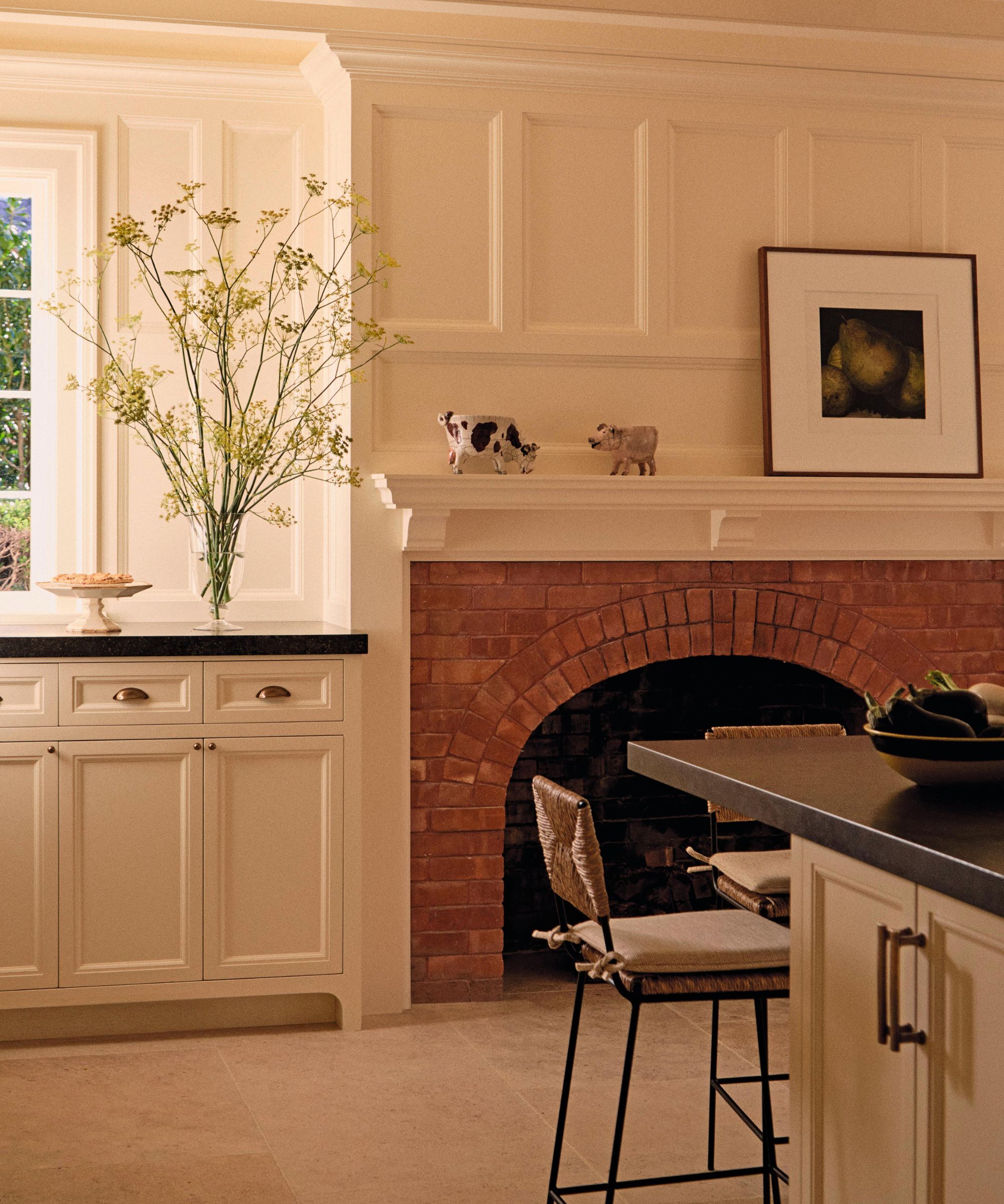 a soft neutral kitchen in the hamptons with a brick fireplace, stone floor and dark stone countertops
