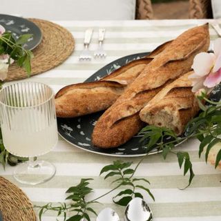 A ceramic dish with baguettes on a striped tablecloth