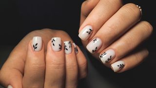 person's hands with white milky nails with a black leaf design