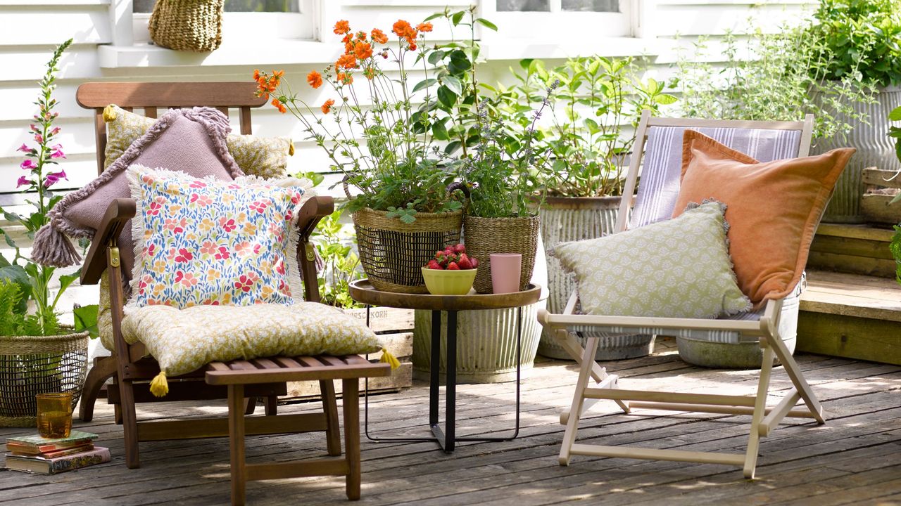 Wooden chairs with patterned cushions and table with potted plants on wooden decking area in garden