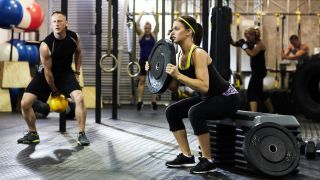 Woman performs a box squat holding a weight plate