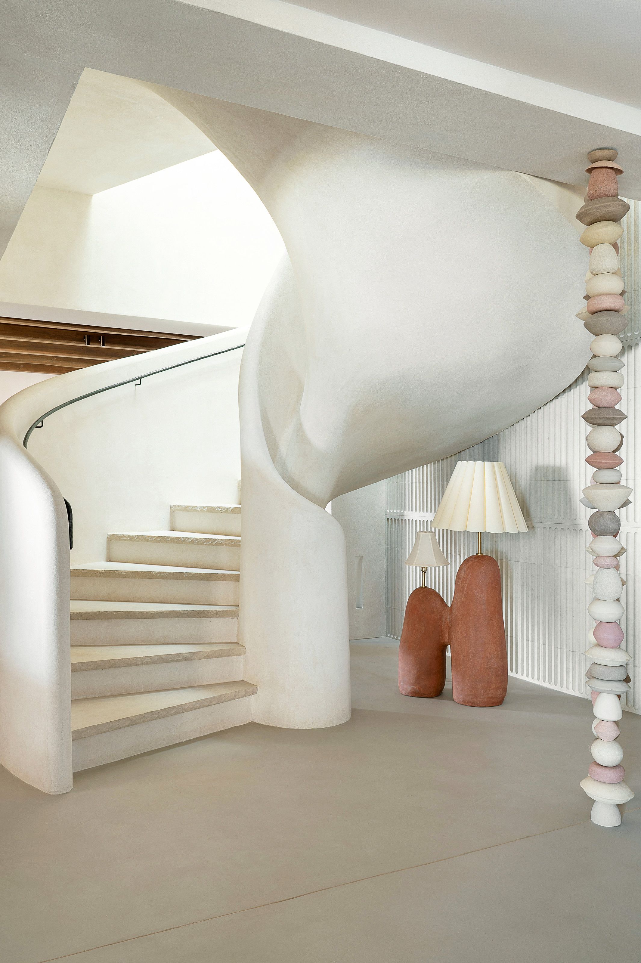 Curved white plaster staircase with a totem-like sculpture and a set of two floor lamps with terracotta base
