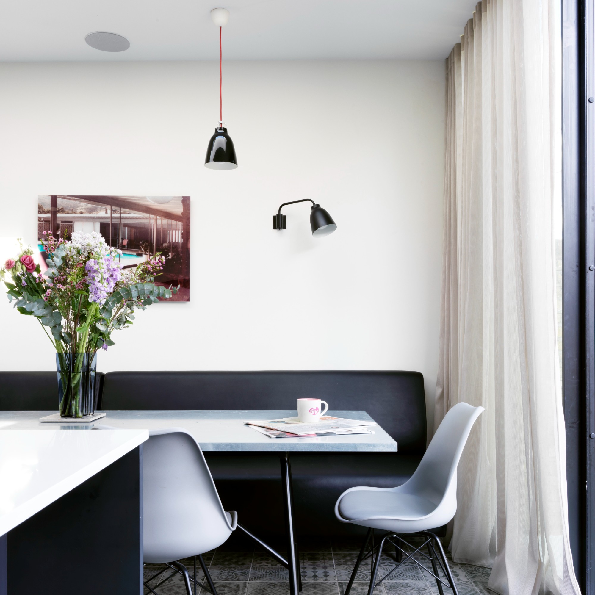A dining area in a white-painted kitchen with a black leather dining bench and a grey dining table and chairs