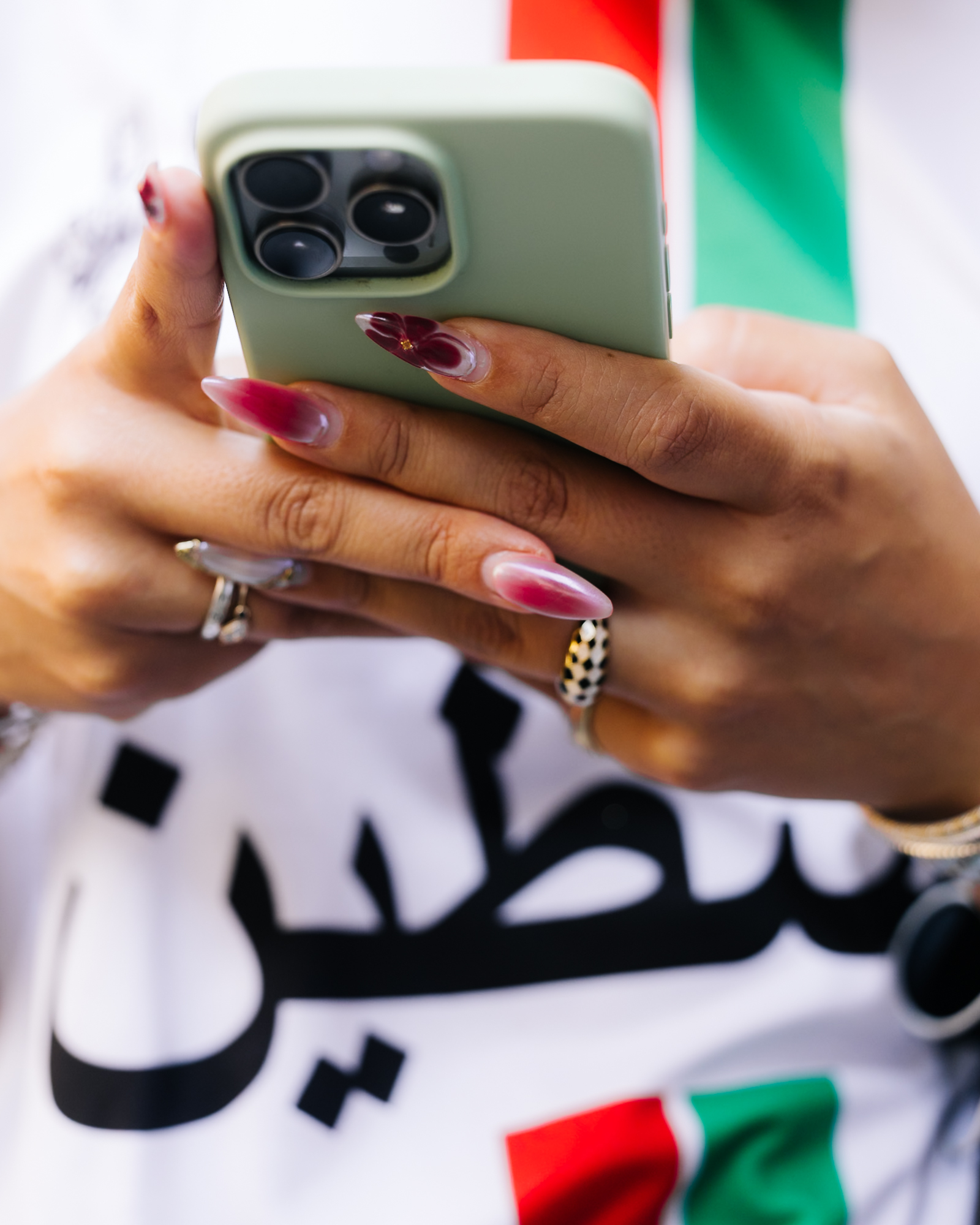 a woman's hands with gold rings and red aura nails holding her phone