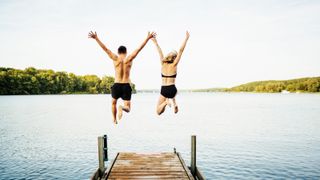 Two friends jumping off a jetty into a lake