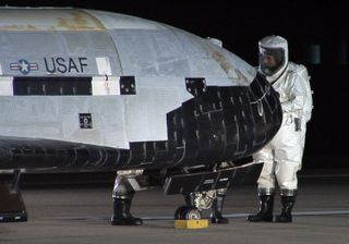 A crew of vehicle handlers clad in suits to protect against hazardous materials (like any remaining rocket fuel) approach the X-37B robot space plane after its successful Dec. 3 landing at Vandenberg Air Force Base in California.