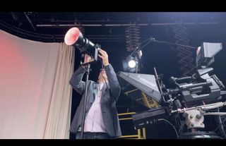 A man adjusting the Neewer CB200C COB RGB LED video light in a tv studio stood next to a teleprompter and camera