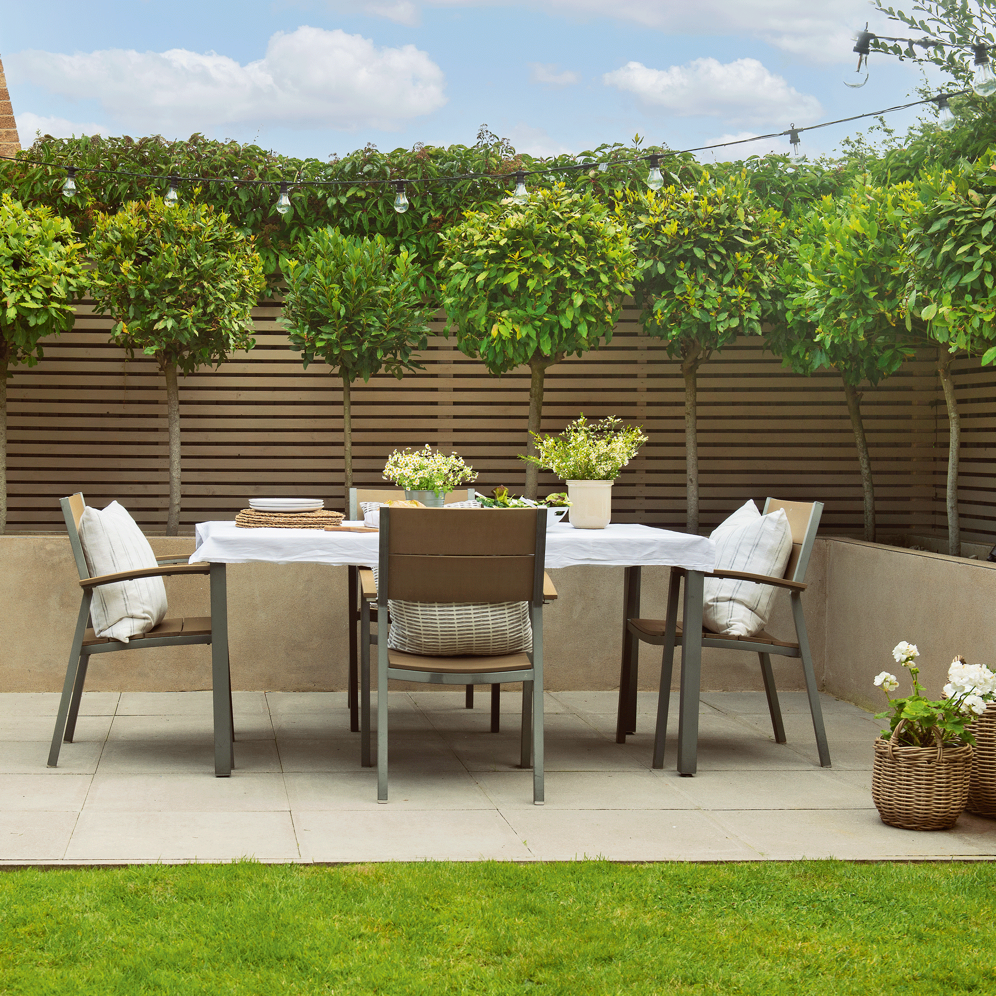 a compact garden with patio and lawn areas horizontal slatted fencing a table and chairs and bay trees planted in raised beds