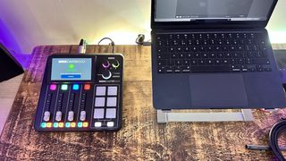 A Rode Rodecaster Duo on a wooden desktop next to a laptop on a stand