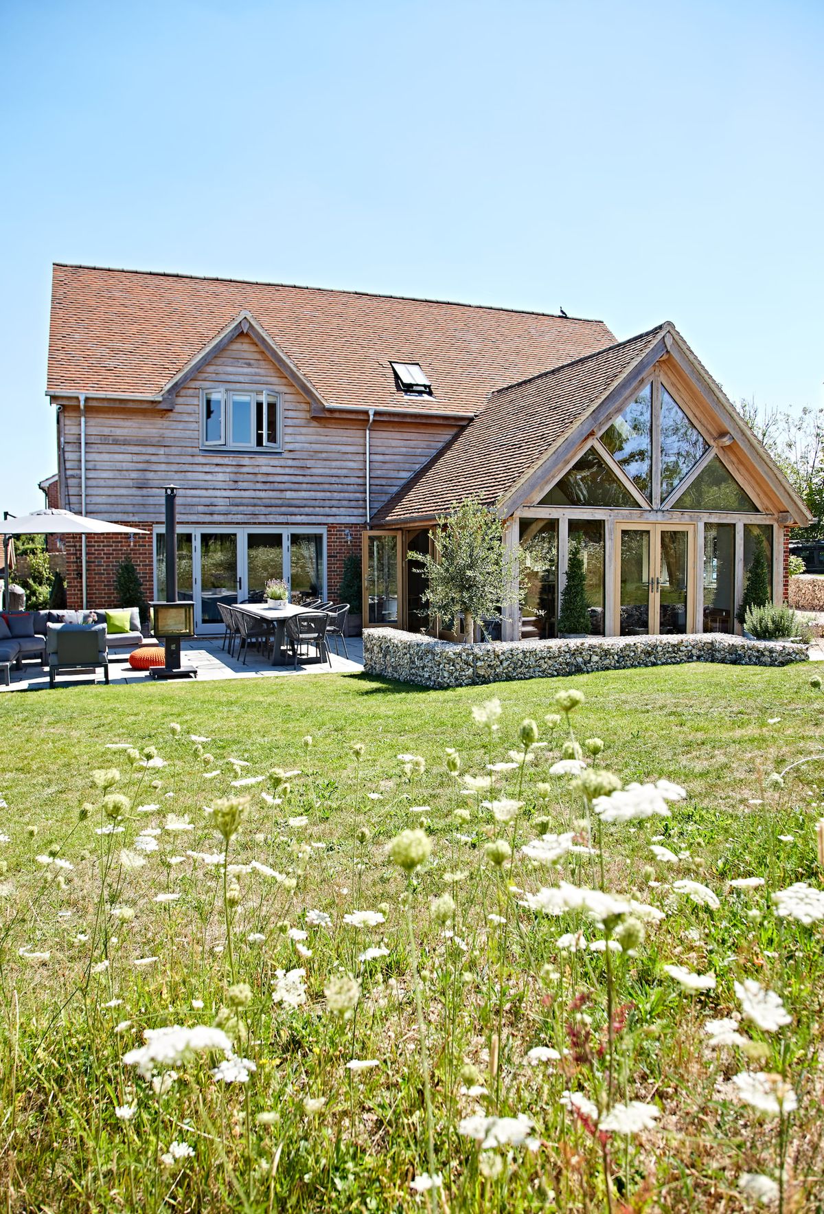 A modern rustic house with a glass and oak frame extension surrounded by meadow gardens