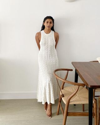 British influencer Monikh Dale wears a textured white sleeveless dress while posing next to her stylish dining room table