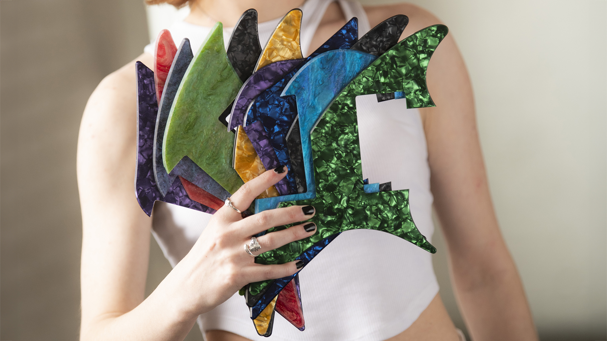 A photo of a woman holding several pickguards for Venus Guitars in an array of colors