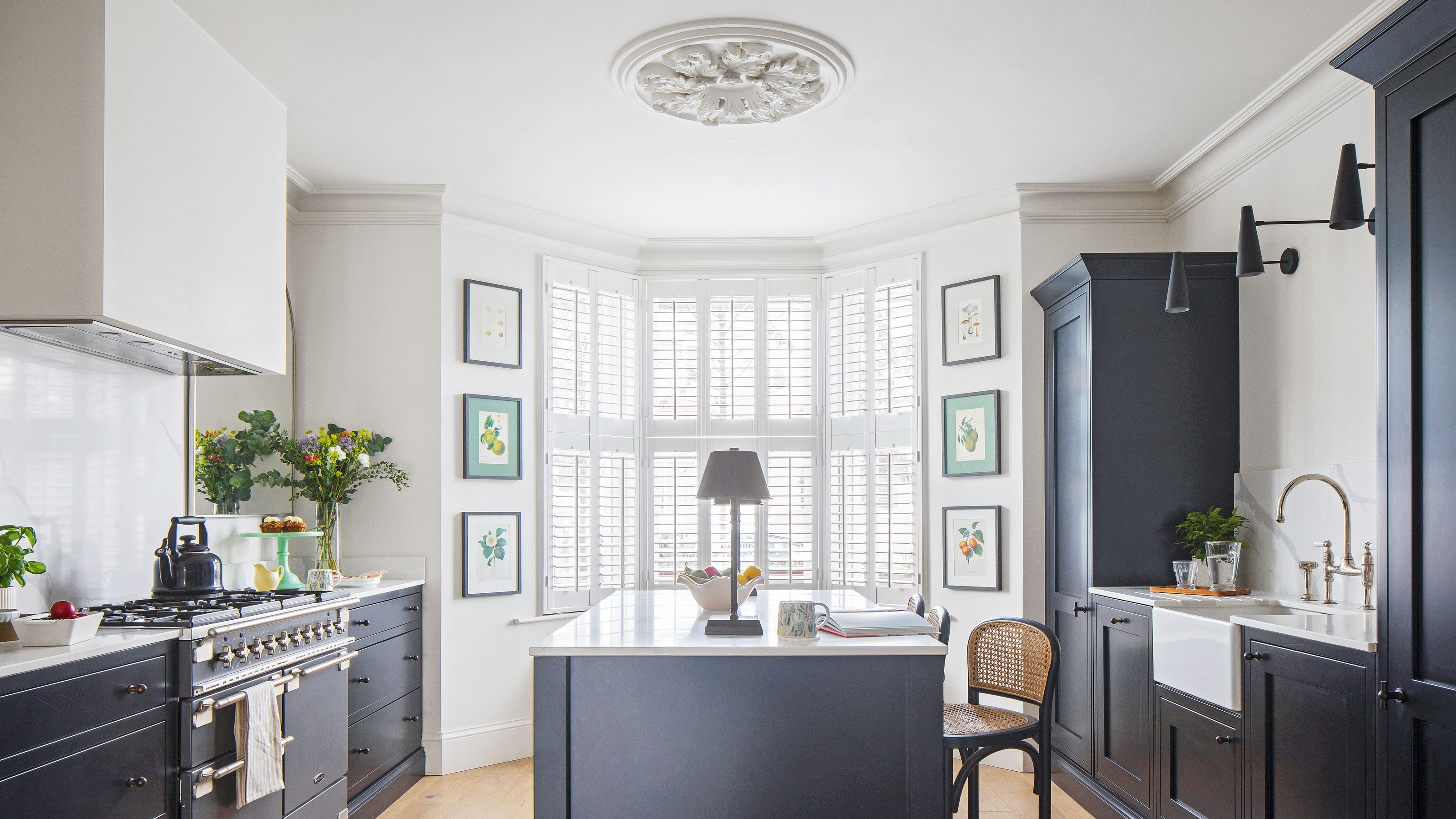 White kitchen walls with navy blue cabinets and a large bay window behind a kitchen island