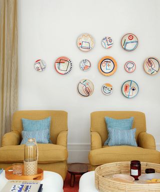 living room with ochre chairs and blue cushions and gallery wall of ceramic plates