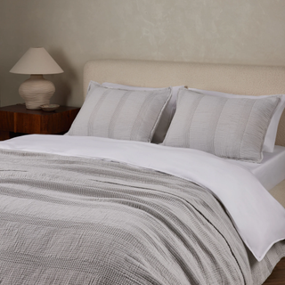 grey bed spread and pillows on a bed with white sheets