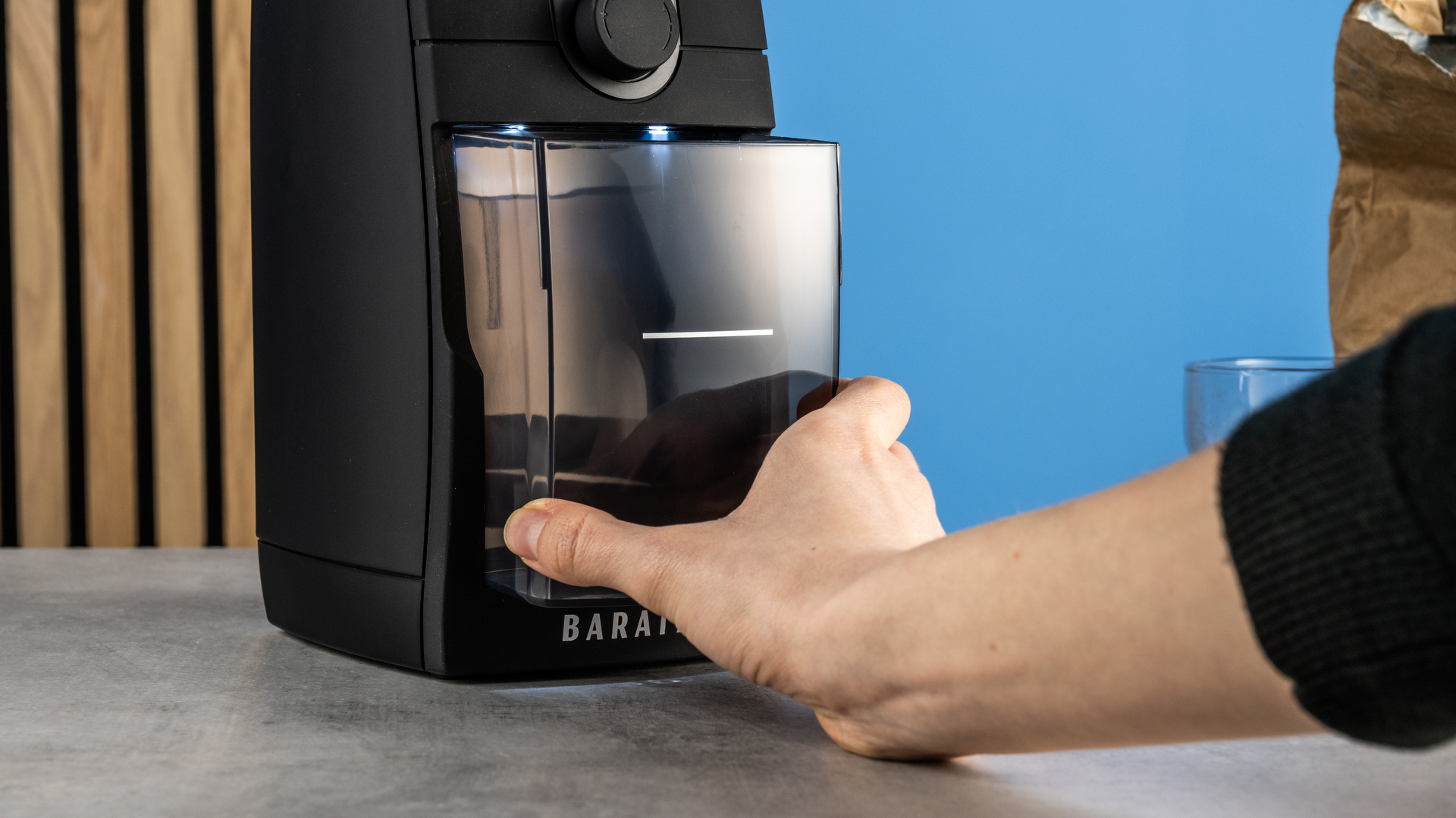 the baratza encore esp pro coffee grinder photographed against a blue tom's guide background with a bag of coffee to the side and showing the grinder in action