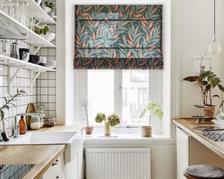 White kitchen with patterned green and orange leaf curtain in window