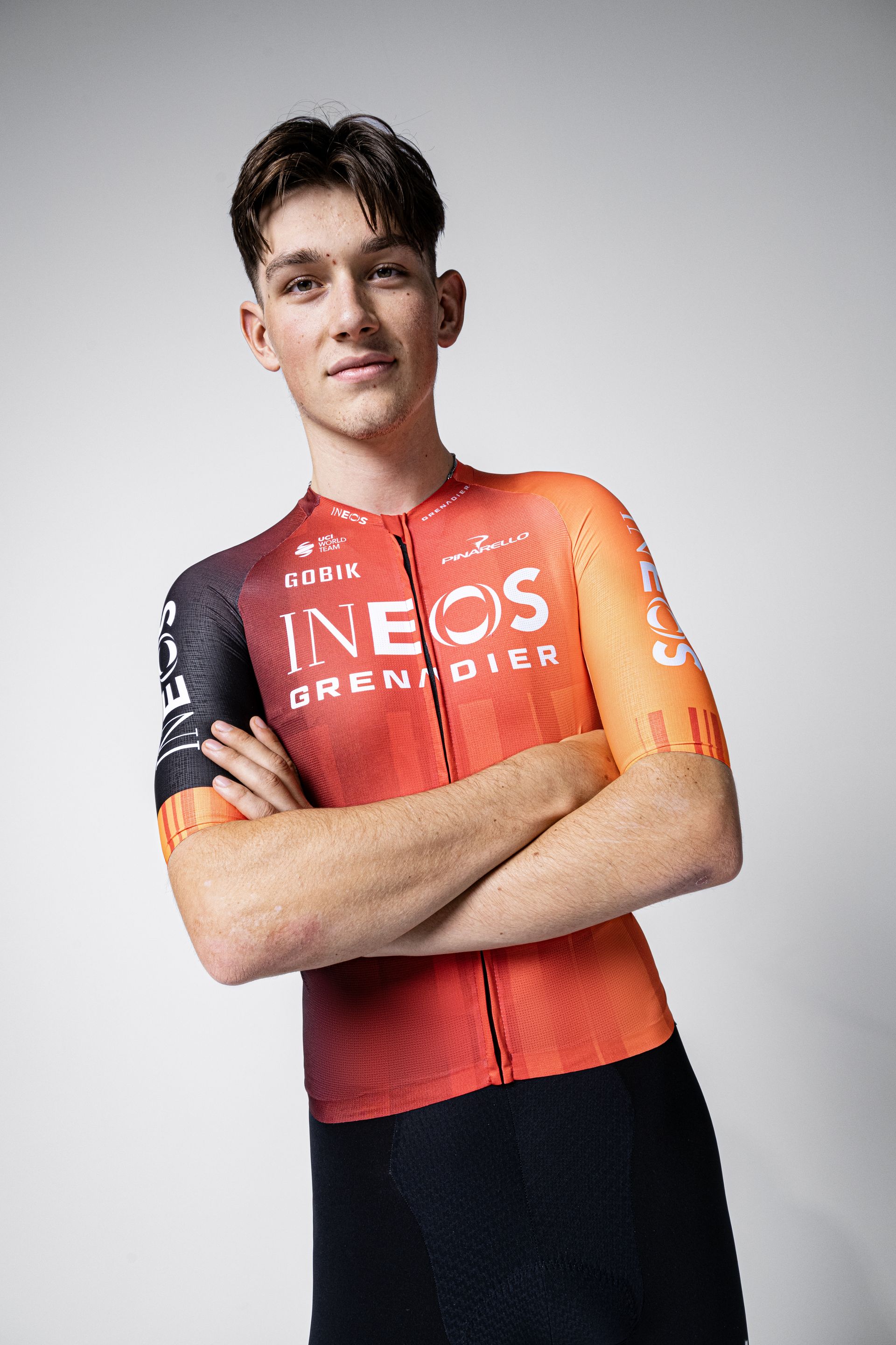 Josh Tarling in the 2025 Ineos Grenadiers kit, a largely red jersey with a dark black right arm, with black shorts