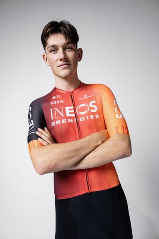 Josh Tarling in the 2025 Ineos Grenadiers kit, a largely red jersey with a dark black right arm, with black shorts