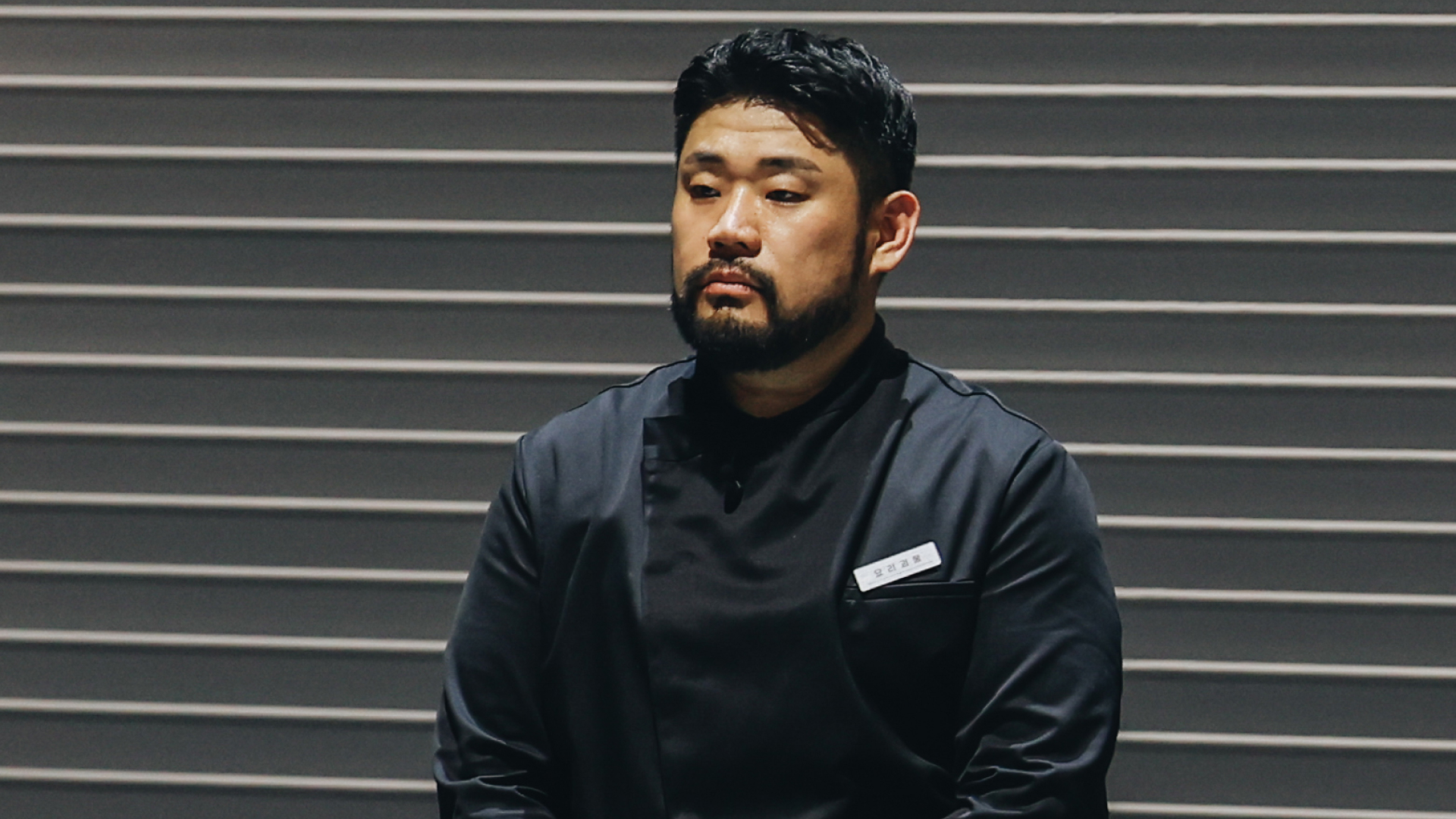 Chef Lee Ha-sung, nicknamed Culinary Monster, stands in front of a wall with horizontal lines, in Netflix's 'Culinary Class Wars.'