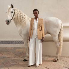 Model wearing Hobbs white and beige suit stood in front of a white horse