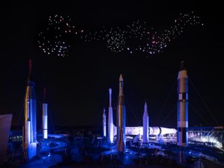 View of the Franchise Freedom installation by Studio Drift featuring multiple illuminated drones flying above multiple Nasa rockets on the ground