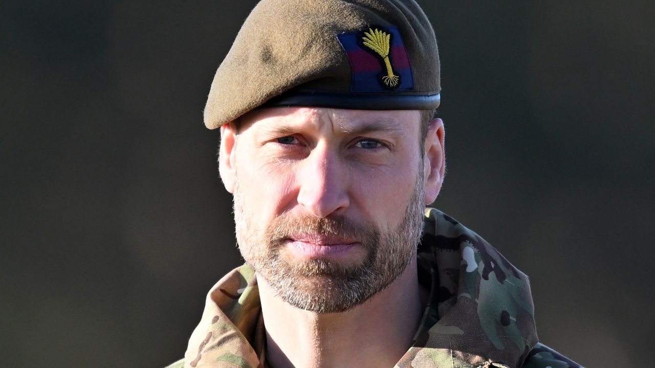 Prince William wearing a camo jacket and green beret looking straight into the camera 