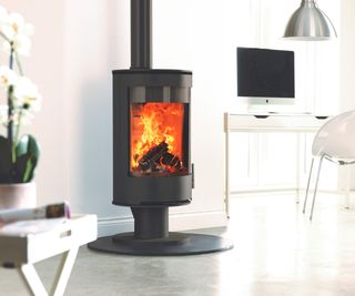 Freestanding circular contemporary woodburning stove, from Charlton & Jenrick, in a white room with a desk