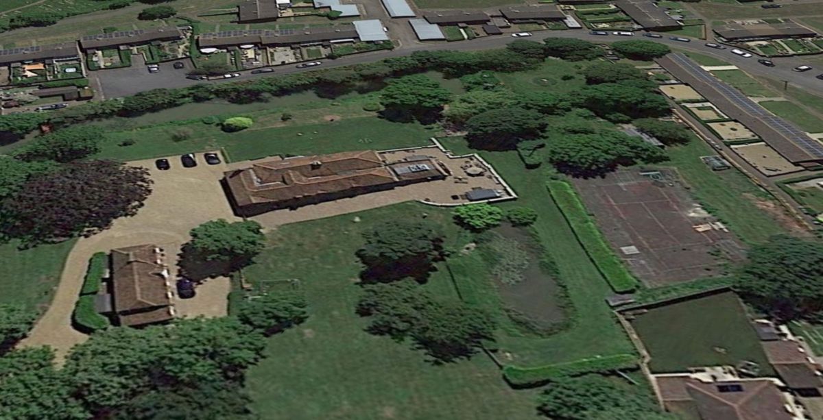 An overhead shot of the plot shows a tennis court surrounded by trees and a main house with a driveway