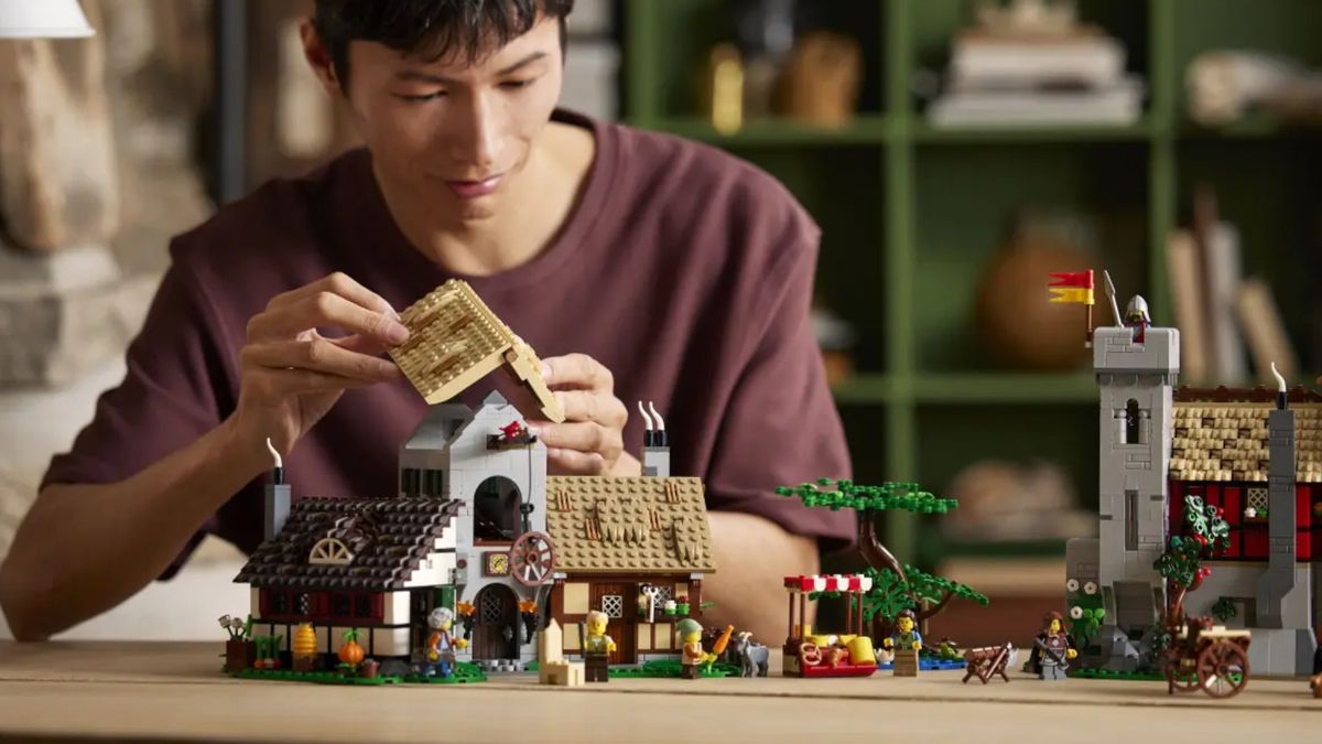 A man puts the roof onto one of the Lego Medieval Town Square buildings