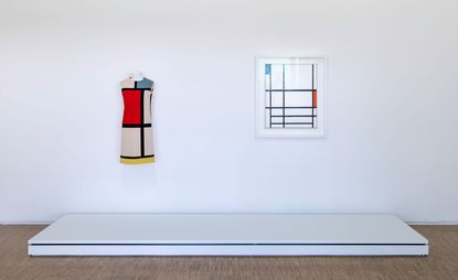 View of Centre Pompidou's tribute to Yves Saint Laurent featuring a colour block dress and wall art on display in a room with white walls, a white platform and wood flooring