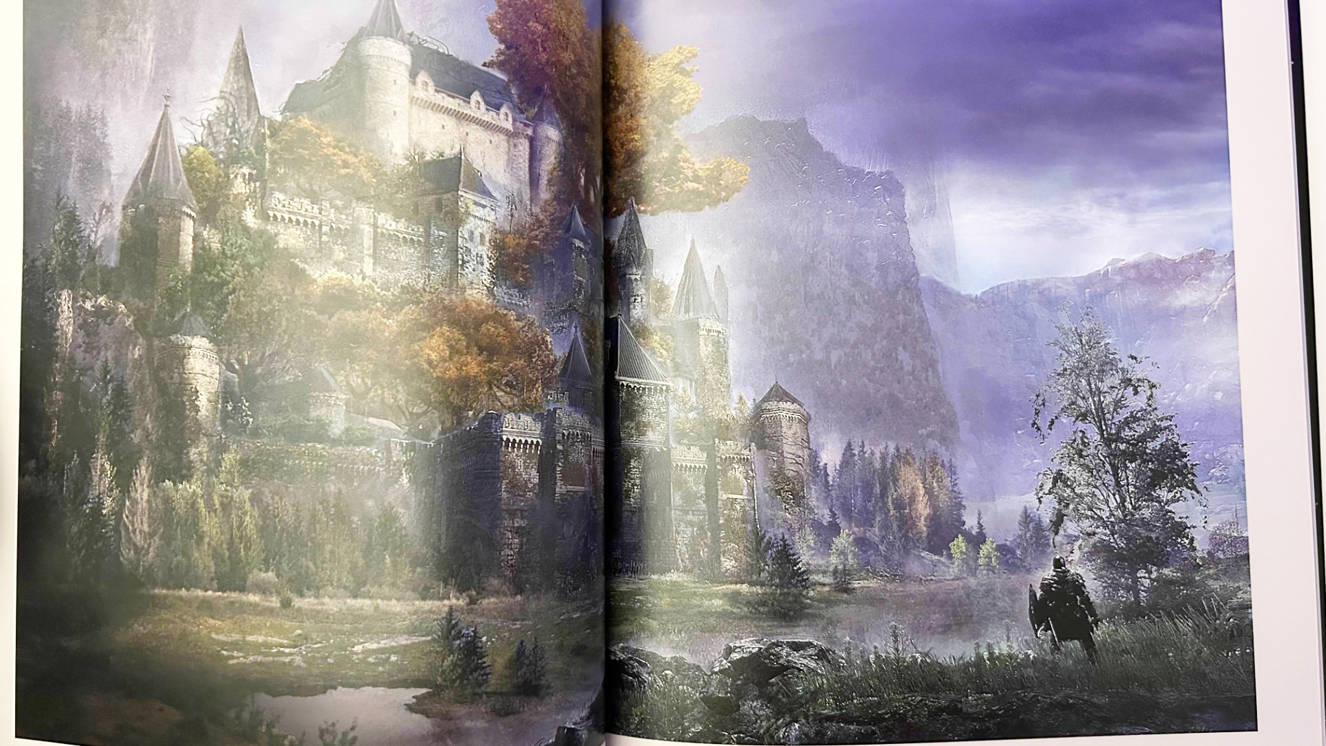 A photo of an Elden Ring concept art book. A large castle sits on a mountain with autumnal trees surrounding it and a lake at the bottom. 