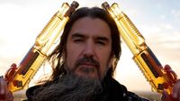 Robb Flynn of Machine Head holding two whiskey bottles shaped like shotguns