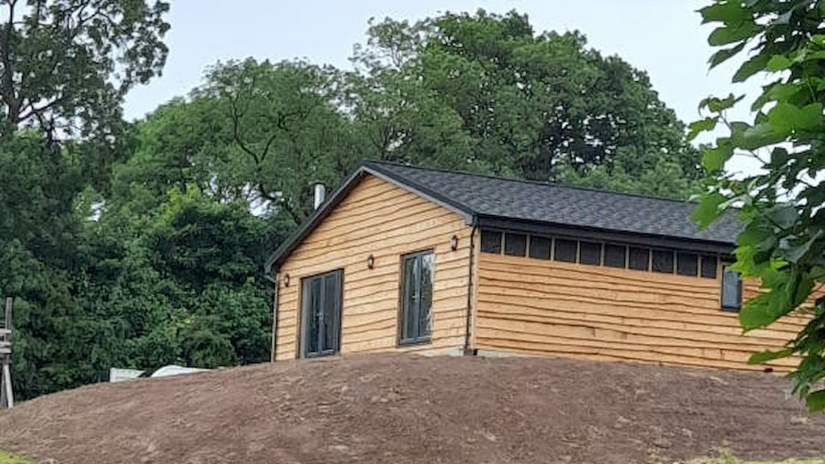 A timber cladded house on farmland on a hill