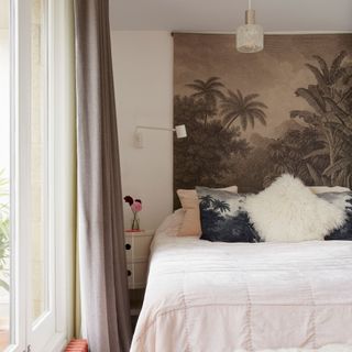 Bedroom with palm tree tapestry hanging over bed with light pink sheets and accent throw pillows