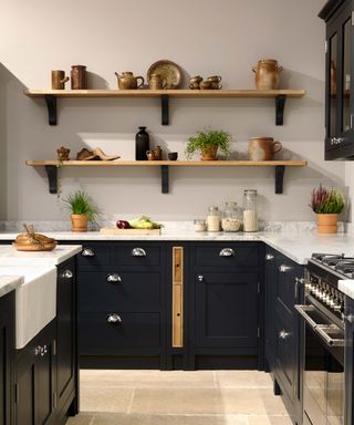 dark blue kitchen with open shelving and oven, dark cupboards and a stone floor