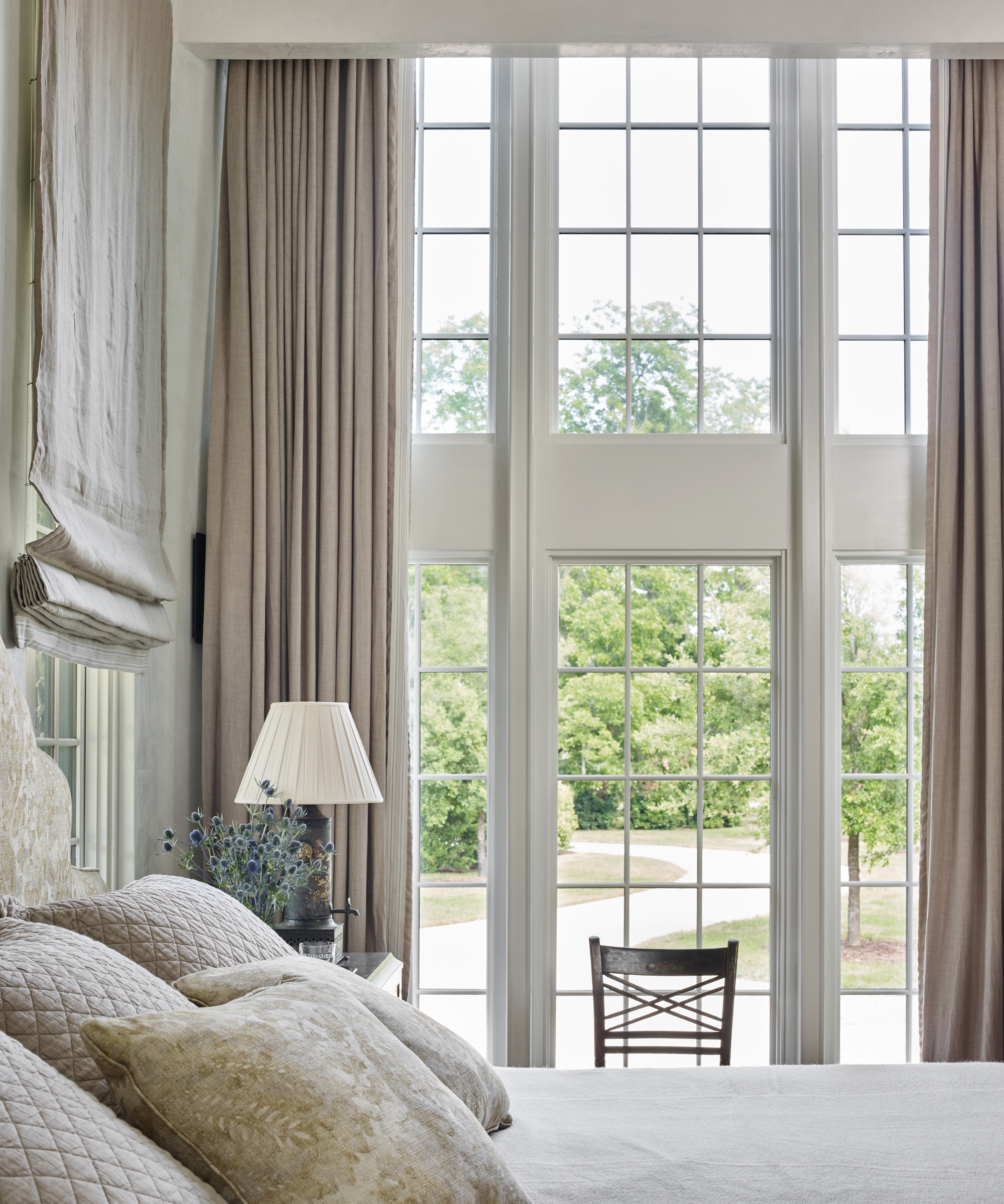 Taupe linen curtains on a large window and a matching blind behind the bed with cushions