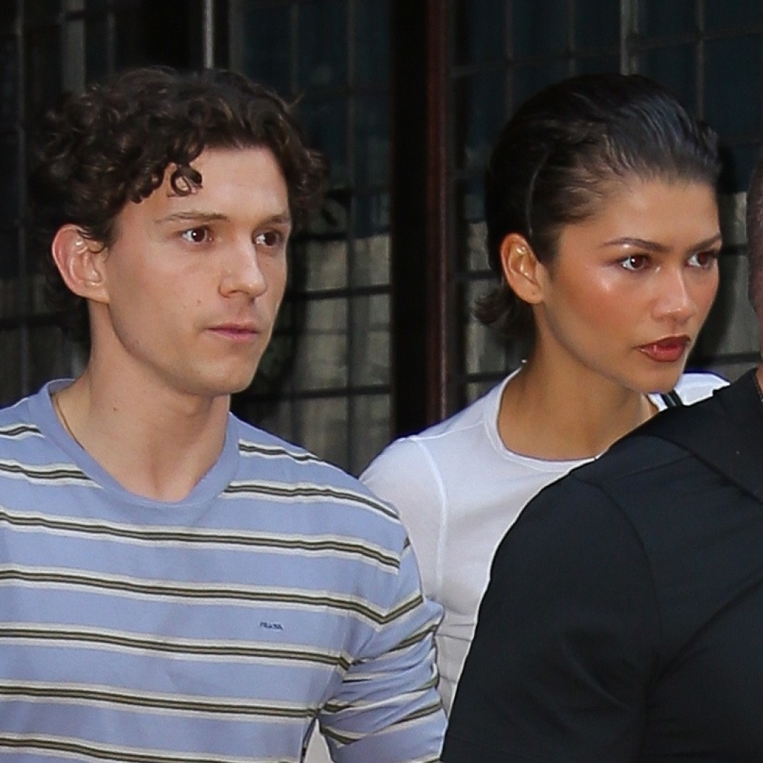 Zendaya wears a white T-shirt and linen pants and has slicked back short hair while holding hands with Tom Holland