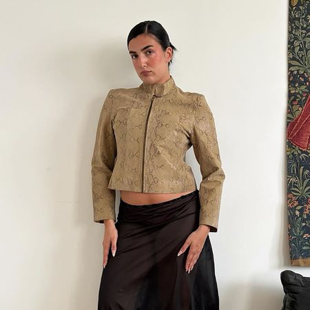 a woman wearing a snakeskin leather zip up jacket, a black sheer skirt, teal tights, and black sandals
