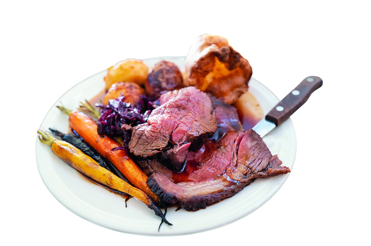 Roast beef on a white plate with roast potatoes and Yorkshire pudding with vegetables in a restaurant.