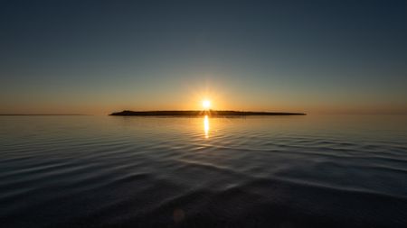 A sunset over a lake with a silhouette of an island right underneath the setting sun