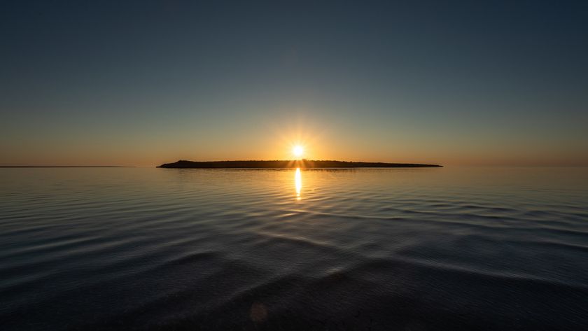 A sunset over a lake with a silhouette of an island right underneath the setting sun