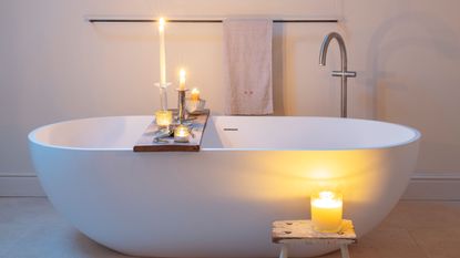 White bathtub in bathroom, bath tray with array of lit candles