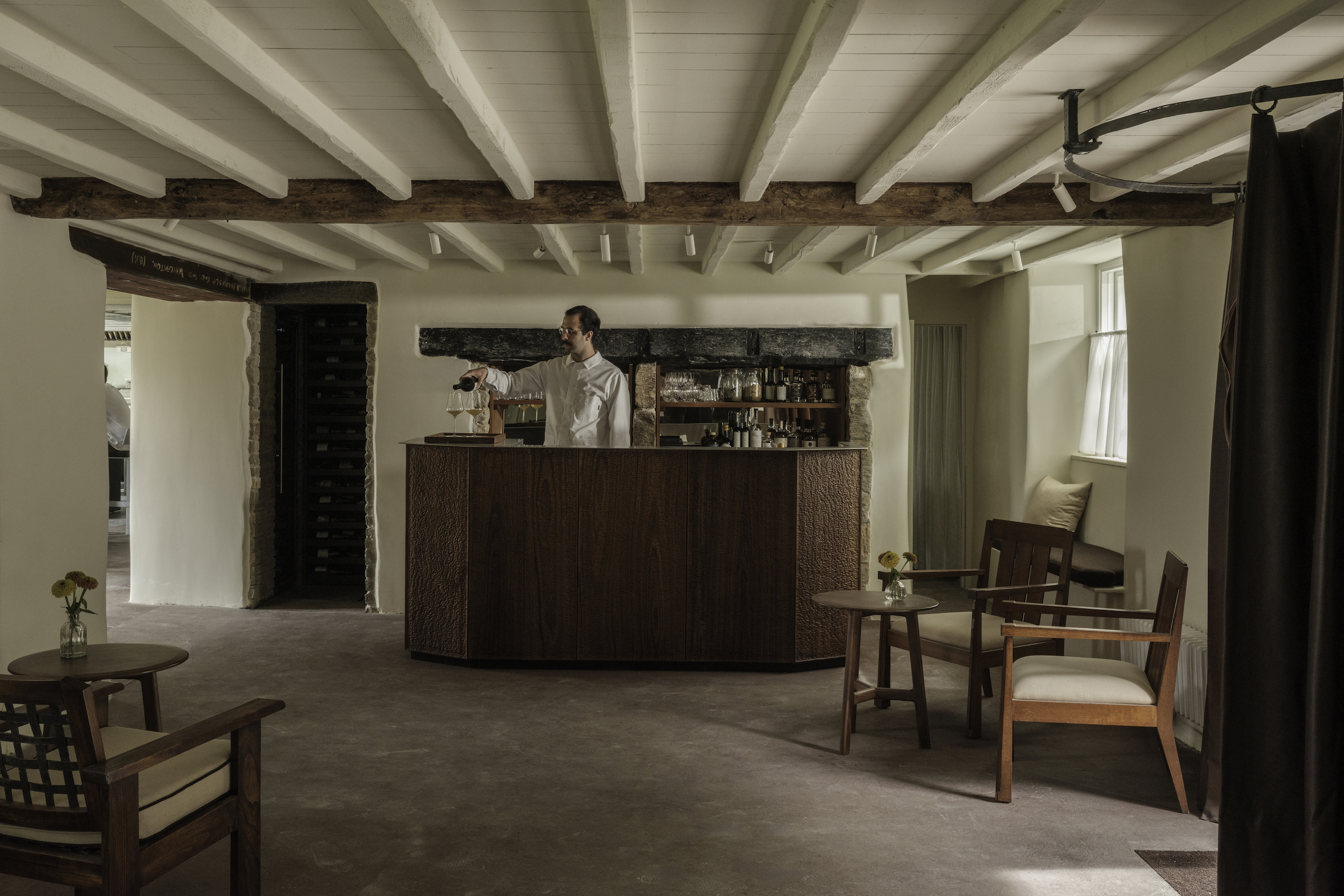 A series of shots depicting the interiors of a modernly renovated, old farmhouse in the countryside, mixing a rustic frame with plush textiles, textural surfaces, glass, wood, and chrome accents, and colorfully plated dishes.